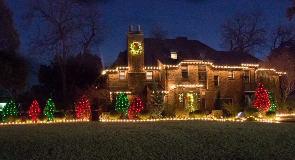 Home with warm white roofline lighting and red and green wreaths on trees