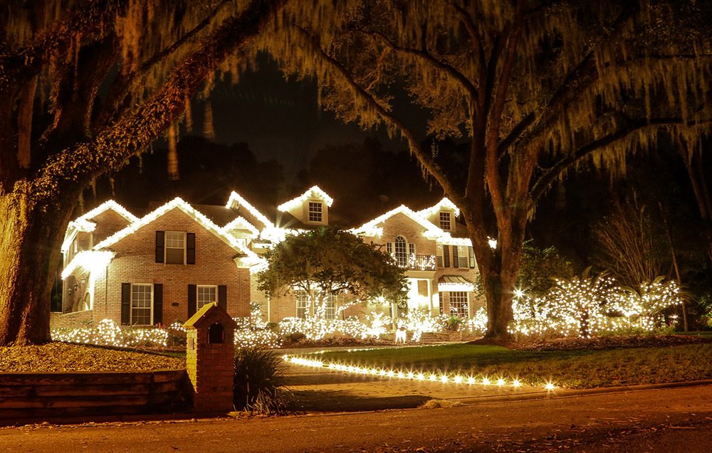 Estate home with warm white roofline lighting under oak trees