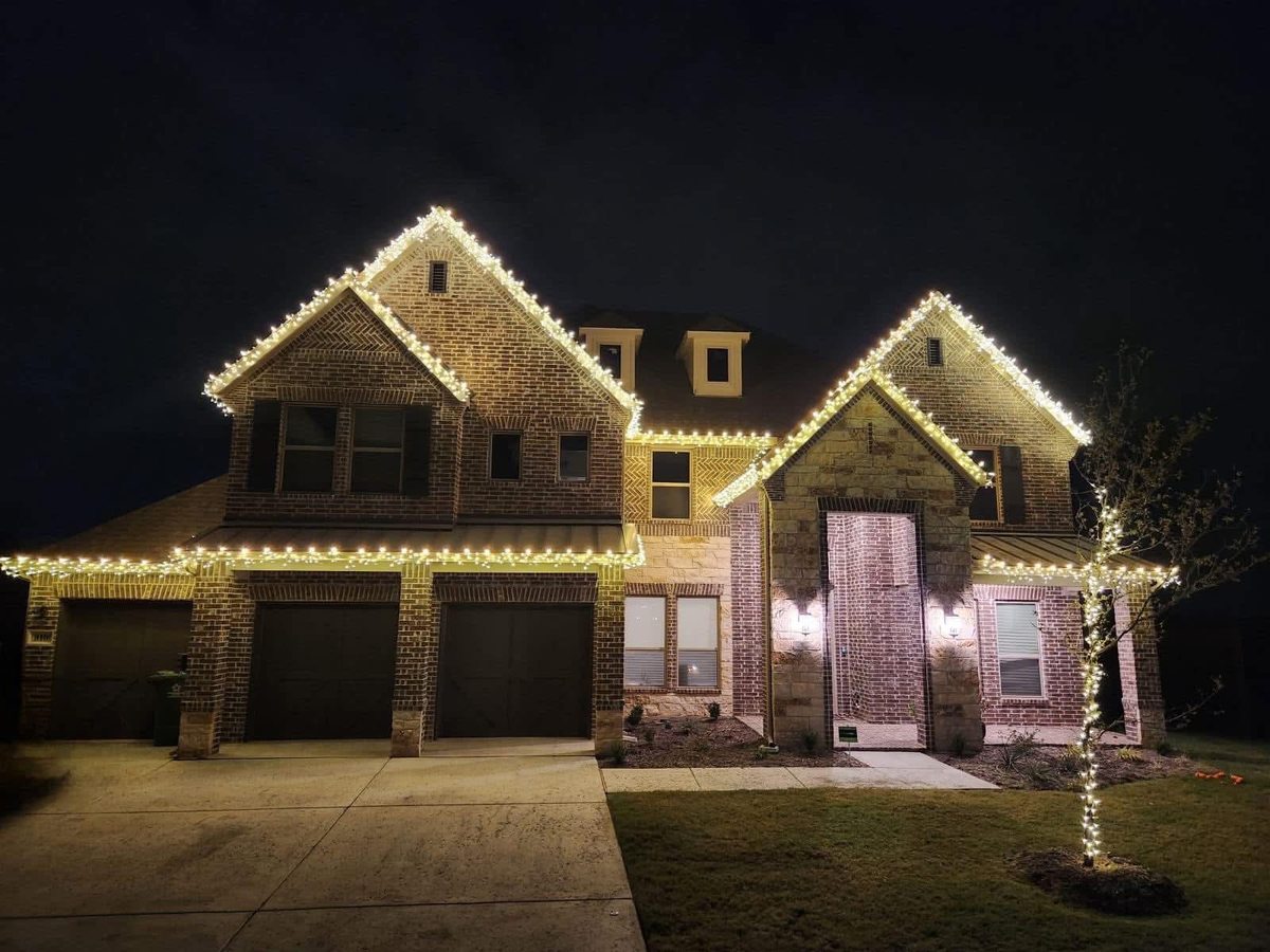 Two-story brick home with warm white roofline lighting and wrapped entry columns
