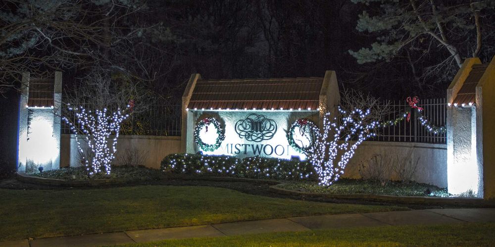 Community entrance sign wrapped in holiday lighting and wreaths