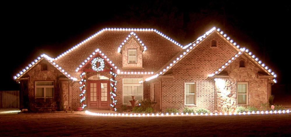 Brick home with warm white roofline Christmas lighting and a wreath